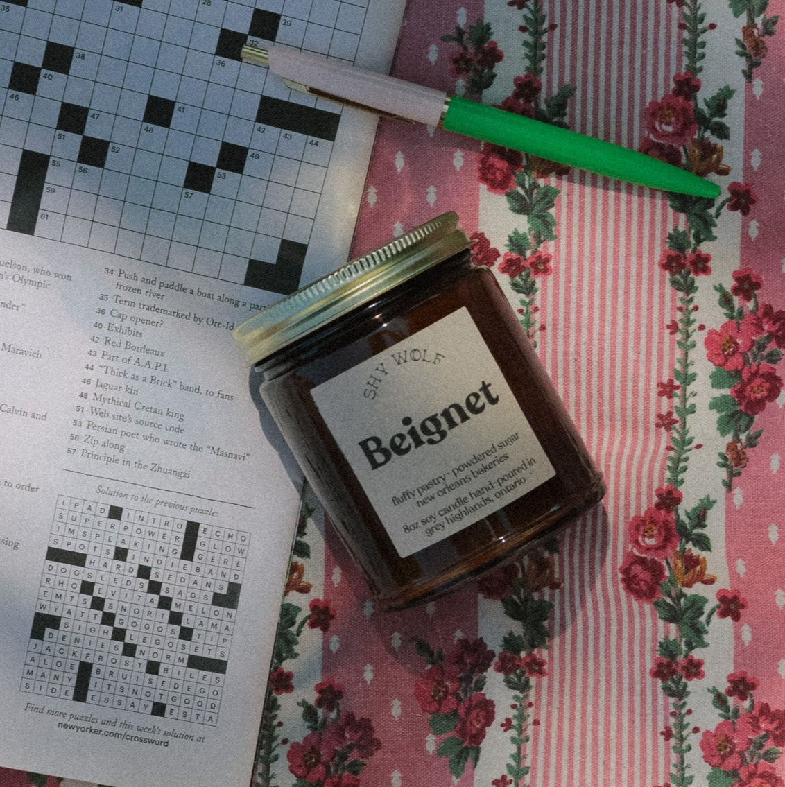 Jar of confiture labeled 'Beignet' on a floral tablecloth with a crossword puzzle